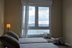 Habitación de hotel con dos camas, una ventana que da al mar, una lámpara y una cortina.