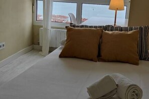 A hotel room with a bed, pillows, a lamp, and a view through a window.