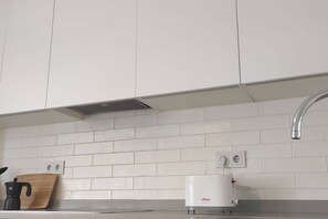 Eine Küche mit weißen Schränken, einer Edelstahl-Spüle, einer Kaffeemaschine und einem weißen Gerät auf der Arbeitsfläche.