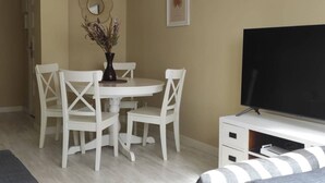 Un comedor con una mesa redonda, sillas blancas, un jarrón con flores secas, un espejo adosado a la pared y un cuadro enmarcado.