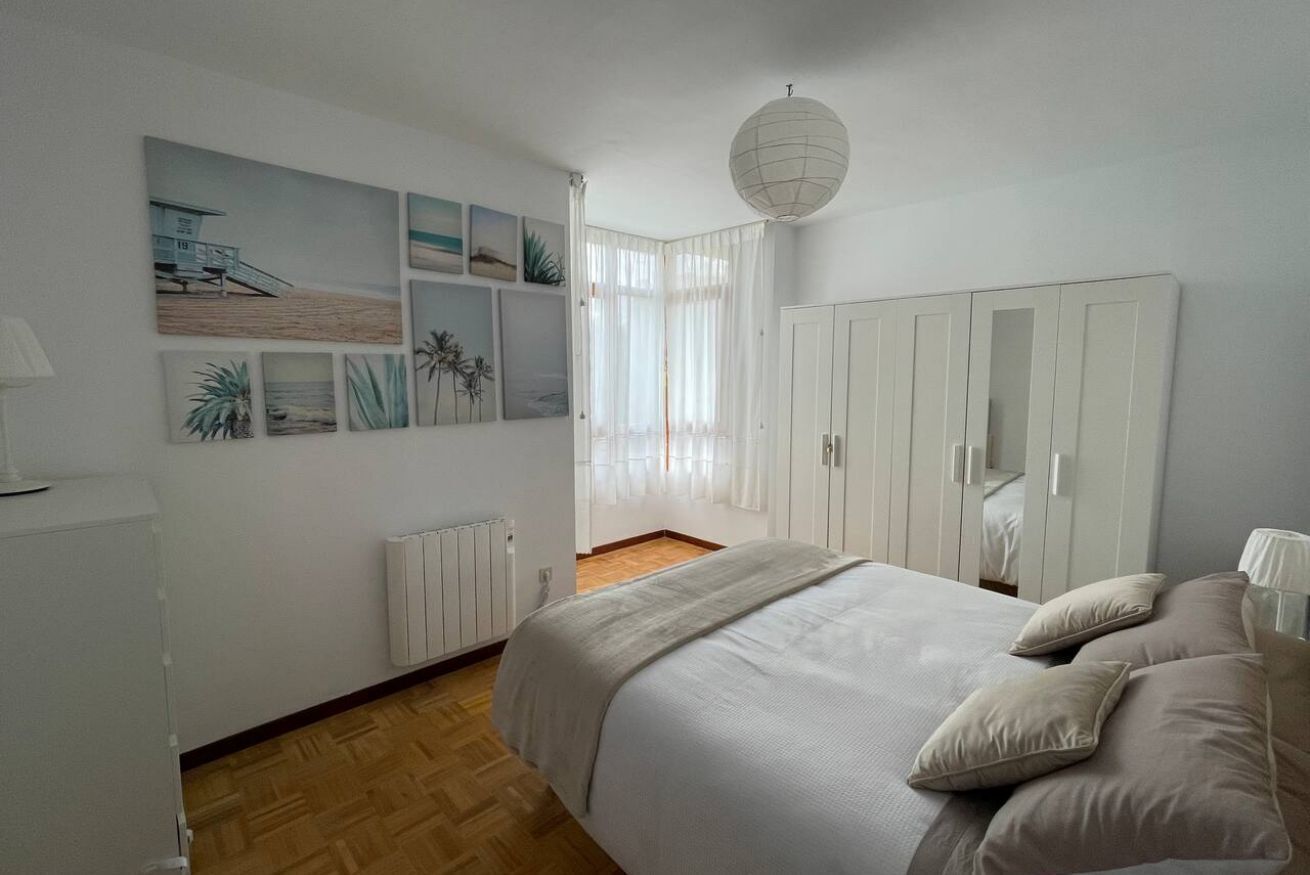 Une chambre à coucher avec un lit, une armoire, un radiateur et une fenêtre ornée de rideaux légers.