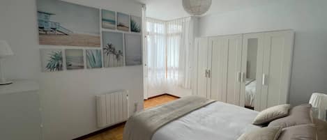 A bedroom with a bed, a wardrobe, a radiator, and a window with sheer curtains.