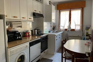 A compact kitchen with a washing machine, stove, microwave, and a dining table with chairs.