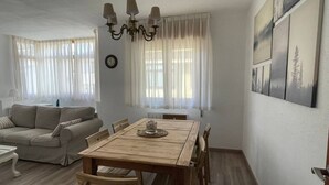 Een woonkamer met een houten eettafel, een beige bank en een kroonluchter.