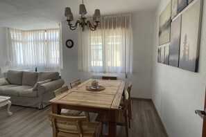 Ett vardagsrum med ett matbord i trä, en beige soffa och en kristallkrona.