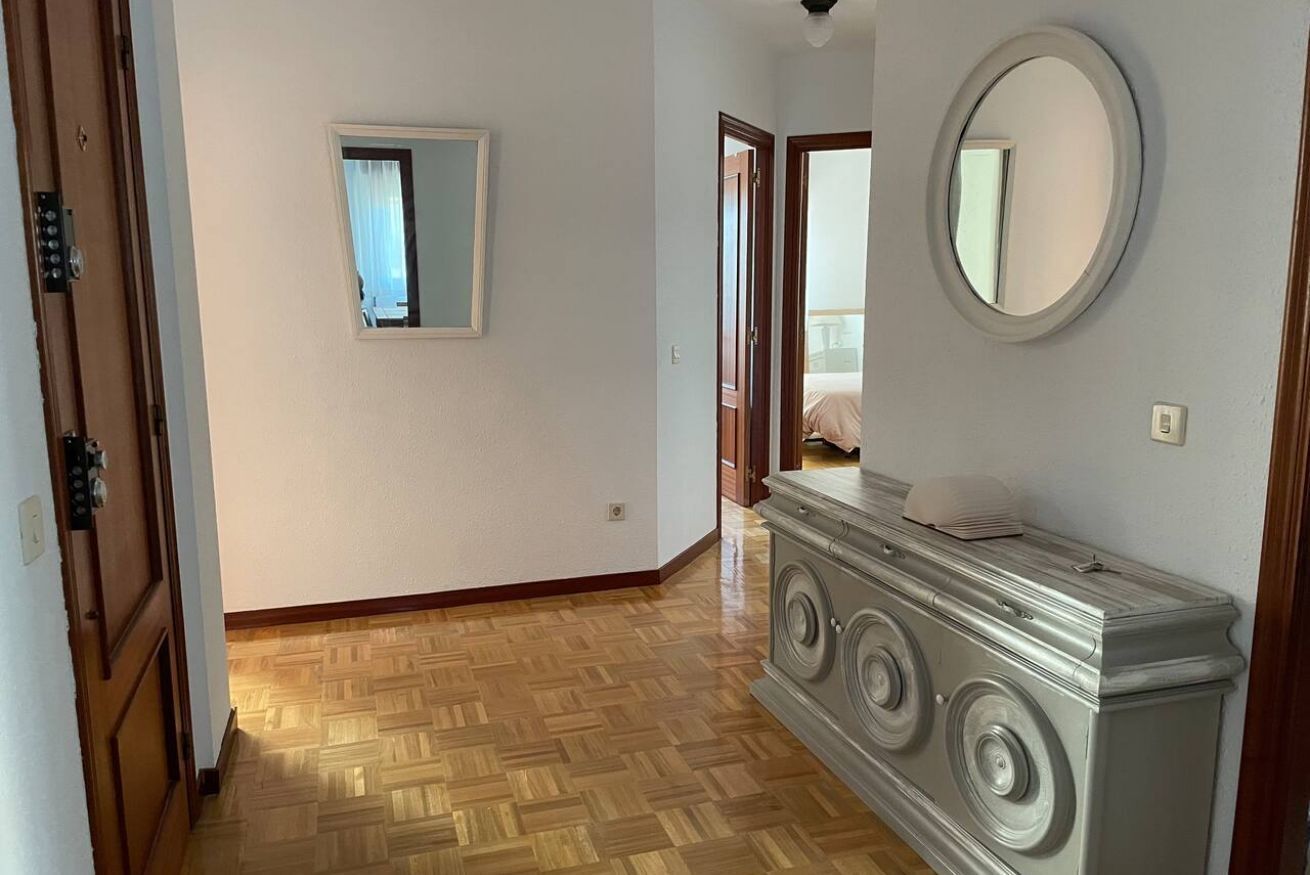 Un couloir avec un plancher en bois, un miroir accroché au mur et une porte donnant sur une autre pièce.