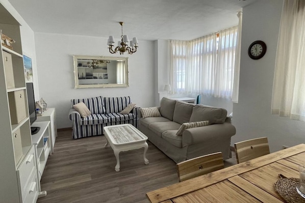 A living room with a striped sofa, a beige sofa, a wooden coffee table, and a dining table with chairs.