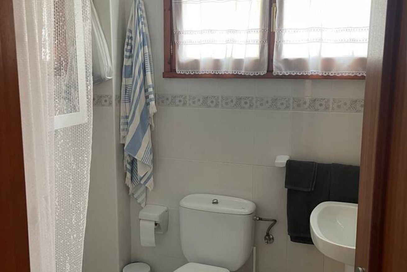 Ein kleines Badezimmer mit Toilette, Waschbecken und einem Fenster mit Vorhang.