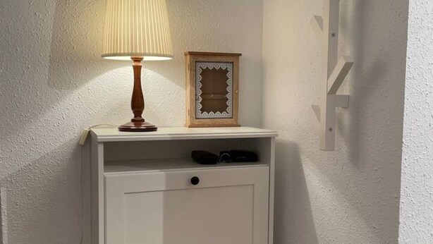 Een witte nachtkastje met een lamp en een decoratieve spiegel.