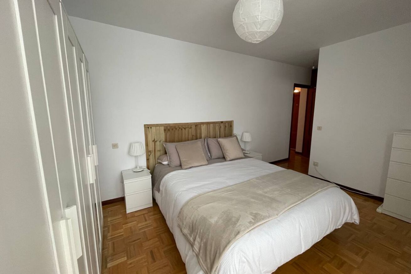 A bedroom with a wooden headboard, a bed with white bedding, a nightstand, a bedside lamp, and a wooden floor.