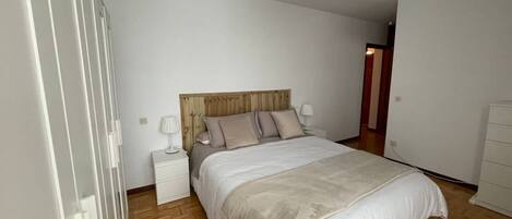 A bedroom with a wooden headboard, a bed with white bedding, a nightstand, a bedside lamp, and a wooden floor.