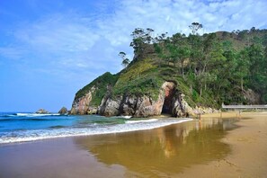 A beach with a rocky cliff, ocean waves, and a clear sky.