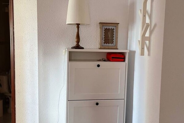 A white bedside table with a lamp, a framed picture, and a red object on top.