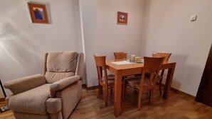 A room with a wooden dining table, four chairs, a beige sofa, and two framed pictures on the wall.