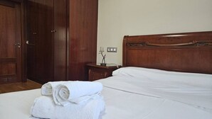 A neatly made bed with white linens, a wooden headboard, and a stack of folded white towels on the floor.