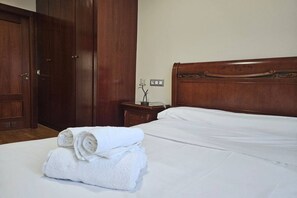 A neatly made bed with white linens, a wooden headboard, and a stack of folded white towels on the floor. - 22A02 Modern Apartment in Arriondas by R2R Consulting (Arriondas)
