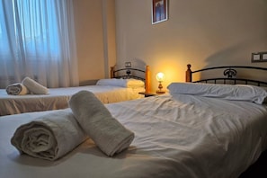 A hotel room with two beds, a bedside lamp, and a window with sheer curtains.