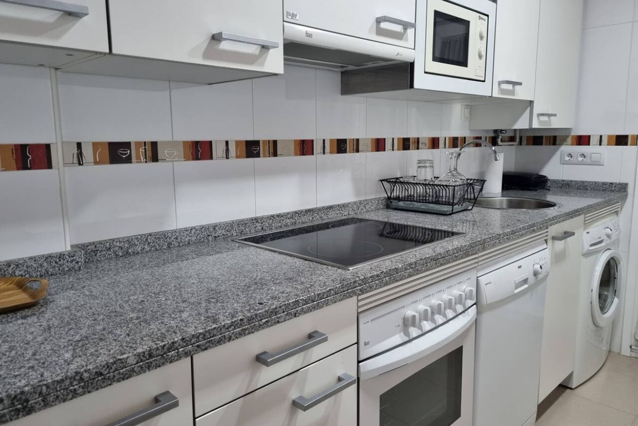 A modern kitchen with a granite countertop, white cabinetry, a built-in microwave, a dishwasher, and a washing machine.