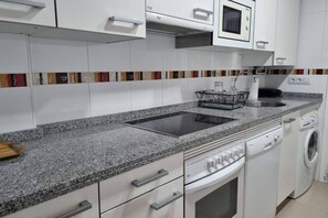 A modern kitchen with a granite countertop, white cabinetry, a built-in microwave, a dishwasher, and a washing machine.