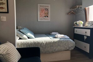 Un dormitorio con cama, cómoda, una obra de arte enmarcada y una lámpara de pared.