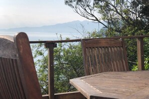 Una mesa y sillas de madera en un balcón con vistas a un cuerpo de agua y montañas.