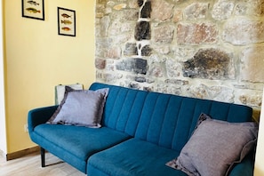 A teal sofa with two pillows against a yellow wall with a stone feature.