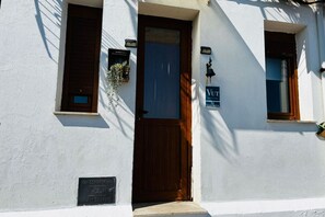 Un edificio con puerta de madera, una ventana pequeña con una planta y un cartel sobre la puerta.