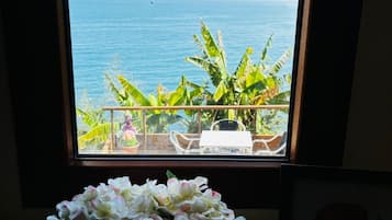 Una habitación con vista al océano a través de una ventana, una planta en maceta y una mesa con sillas.