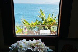 Una habitación con vista al océano a través de una ventana, una planta en maceta y una mesa con sillas.