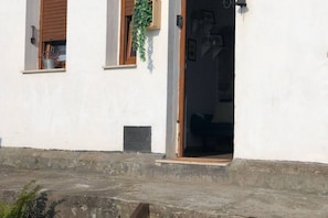 A building with a white exterior, a wooden door, and a window with a plant. - The LLastrina 14A03 by R2R Consulting (Lastres)