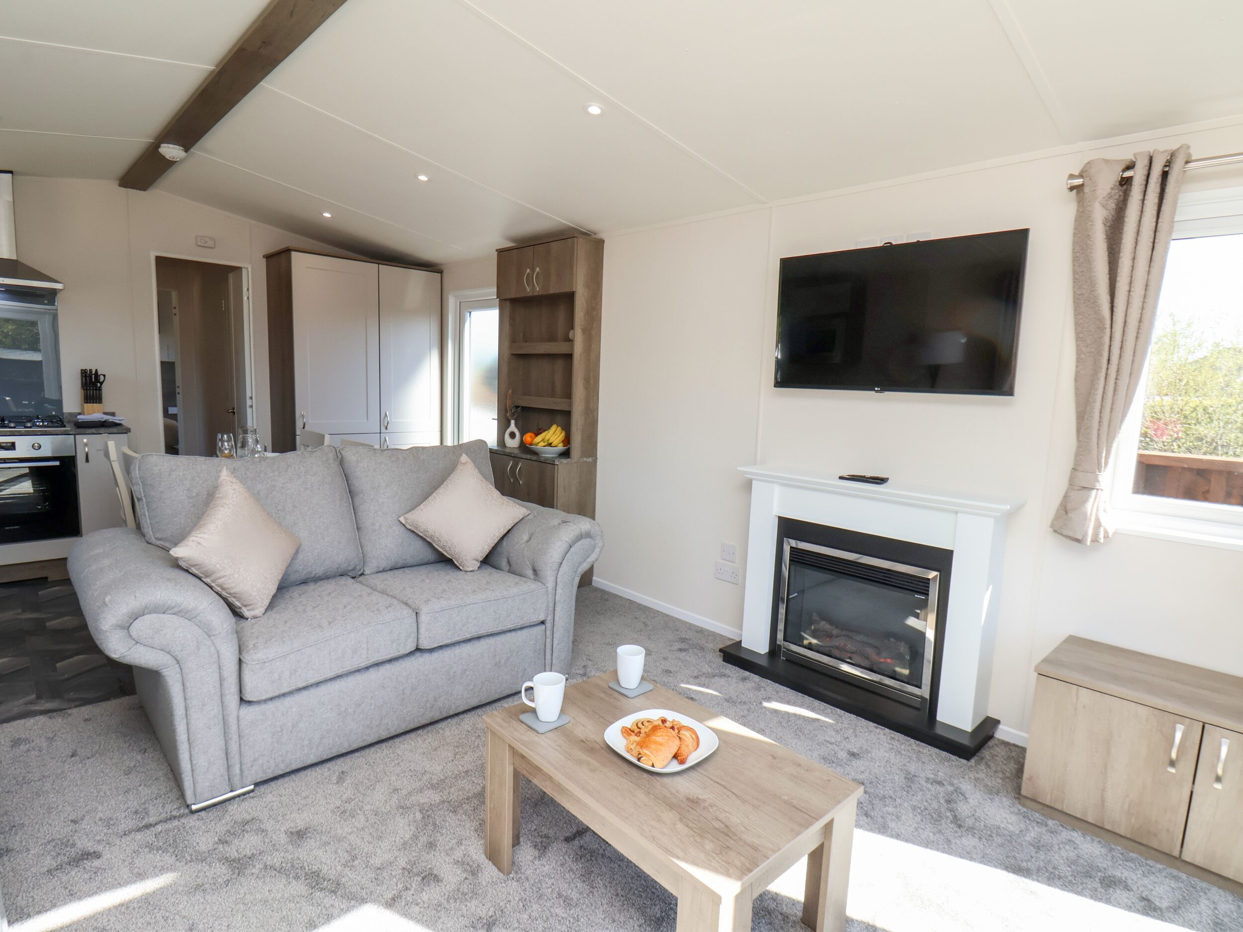 A living room with a grey sofa, a wooden coffee table, a fireplace, and a kitchen in the background.