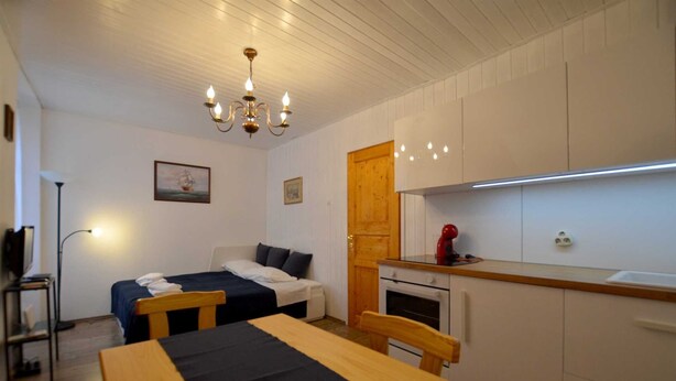 Una habitación pequeña con cama, una mesita, kitchenette y una lámpara en el techo.