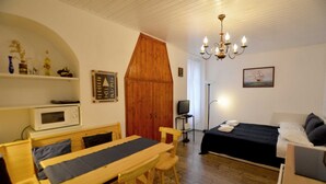 Una habitación de hotel pequeña con una mesa de comedor de madera, una cama con cubierta oscura, un televisor y una araña.