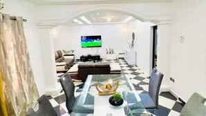 Ein modernes Wohnzimmer mit Schachbrettmuster-Boden, einem Glastisch und einem an der Wand montierten Flachbildfernseher.