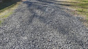 A gravel driveway leading to a building with a small shed and a blue chair in the background.