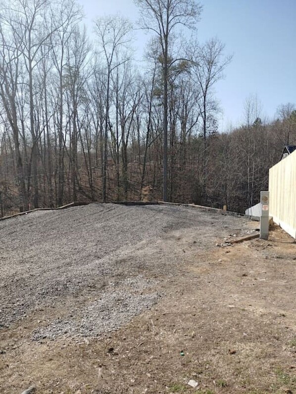 A gravel yard with a wooden fence and trees in the background.