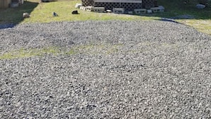 A small wooden cabin with a metal roof, surrounded by a gravel driveway and sparse grass.