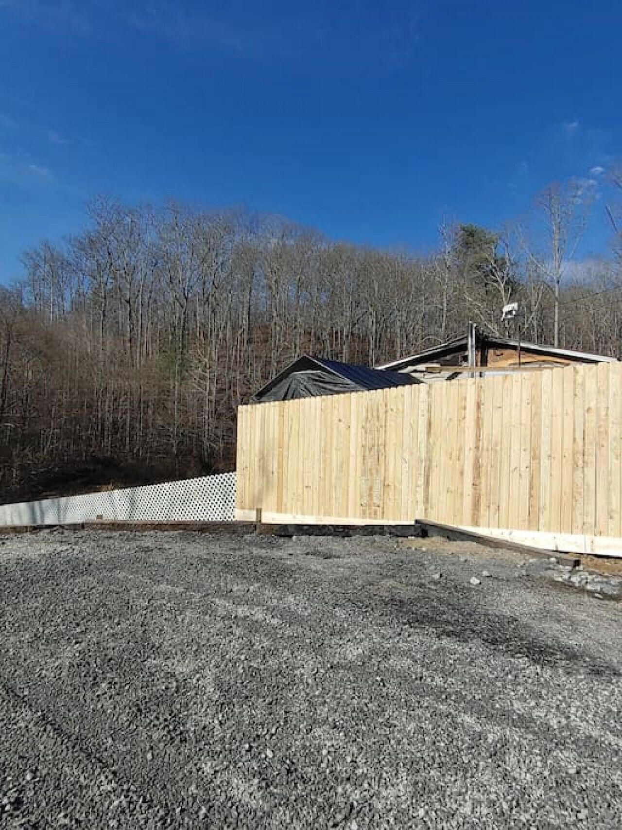 A wooden building with a sloped roof, surrounded by a gravel area and a fence.