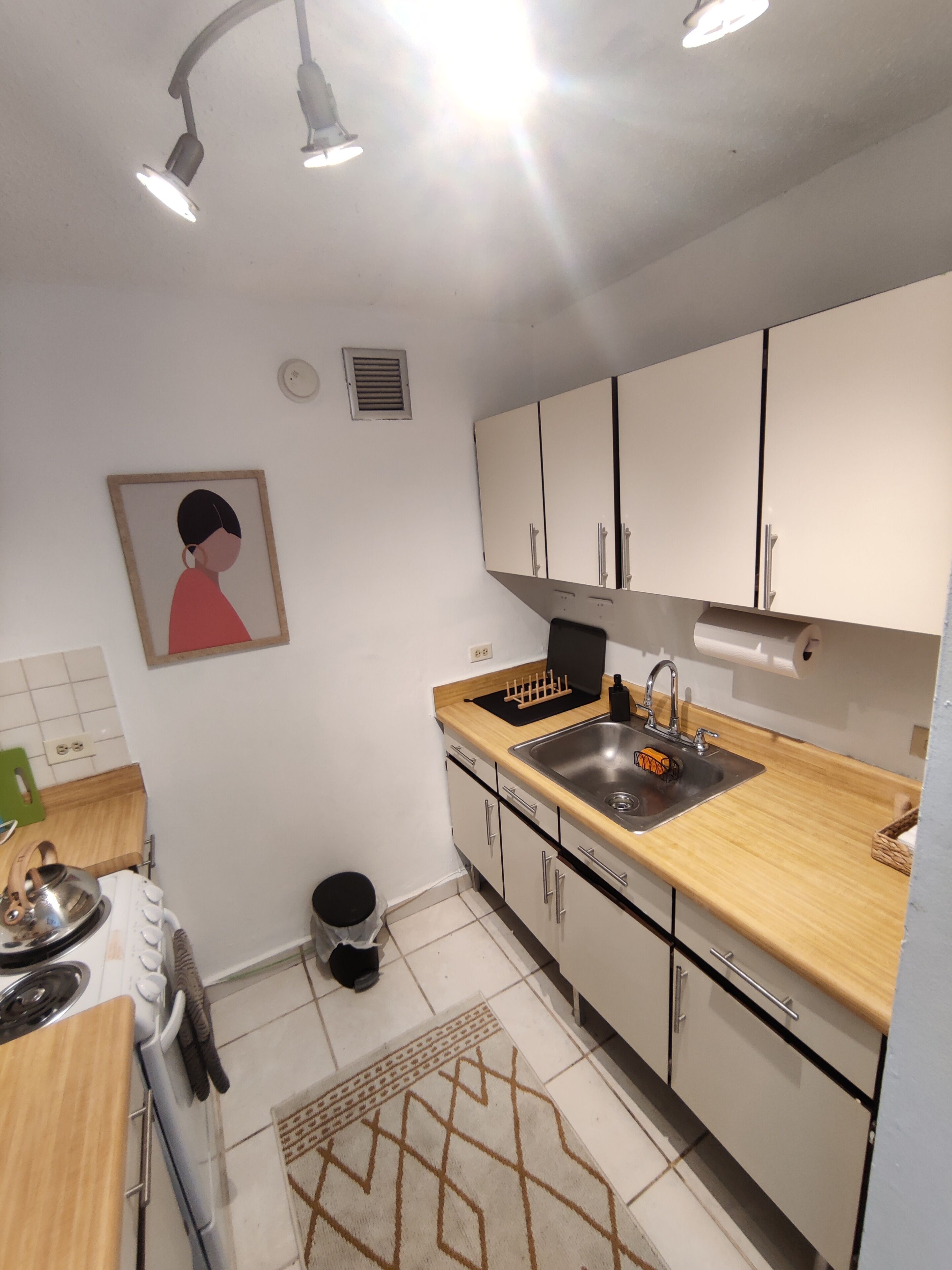 A modern kitchen with white cabinets, a wooden countertop, a stainless steel sink, and a gas stove.