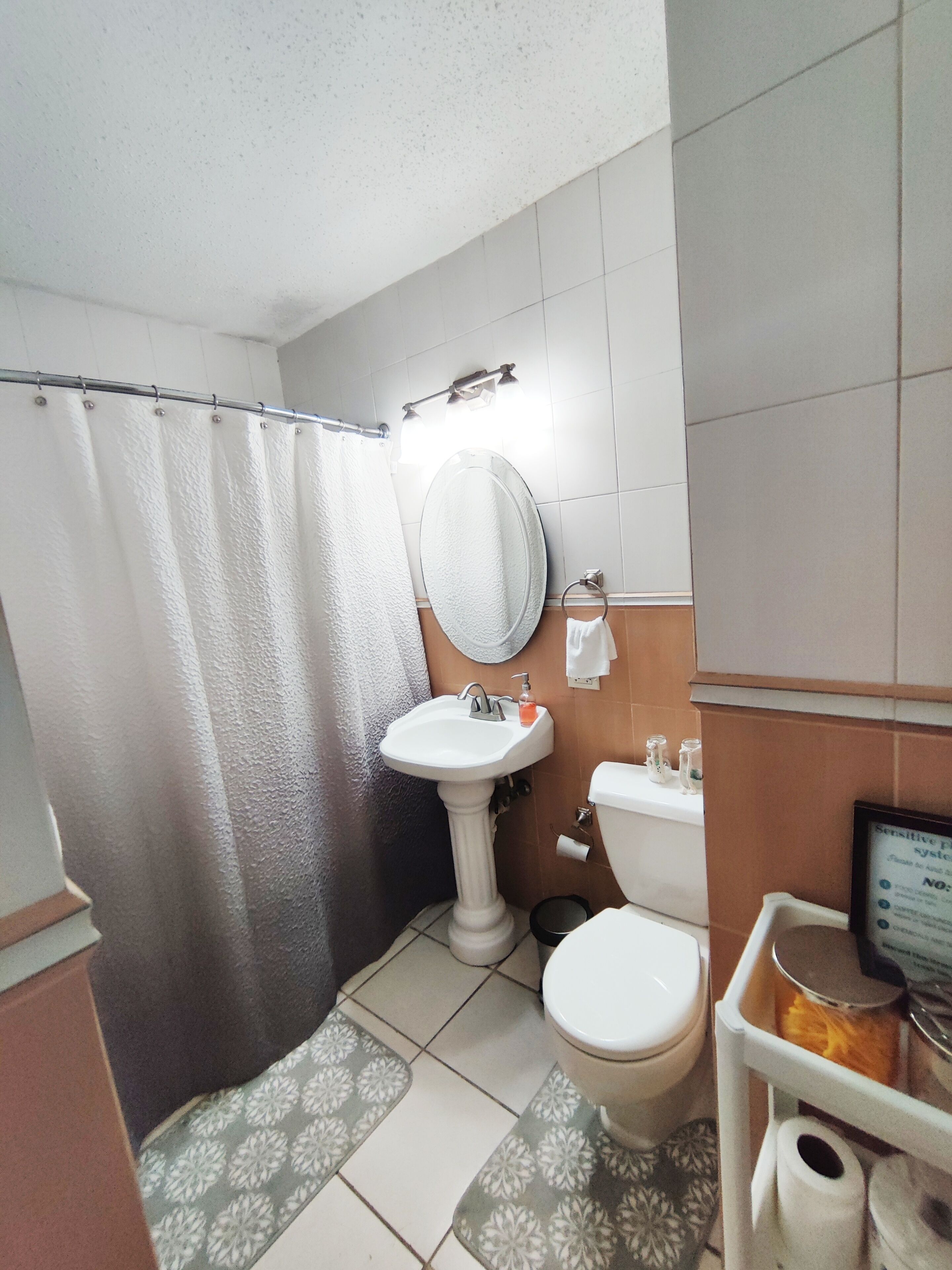 A bathroom with a shower curtain, sink, toilet, and a small shelf with toiletries.