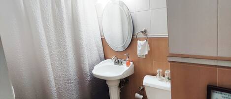 A bathroom with a shower curtain, sink, toilet, and a small shelf with toiletries.