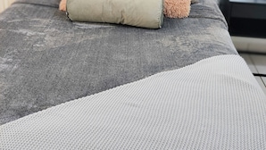 Un letto rifatto con cura, coperto da una coperta grigia a righe bianche, due cuscini soffici e una coperta arrotolata di lato.