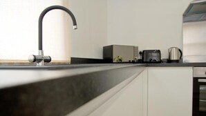 Moderni keittiö, jossa on tyylikäs musta työtaso, ruostumattomasta teräksestä valmistettu hana, leivänpaahdin ja vedenkeitin.