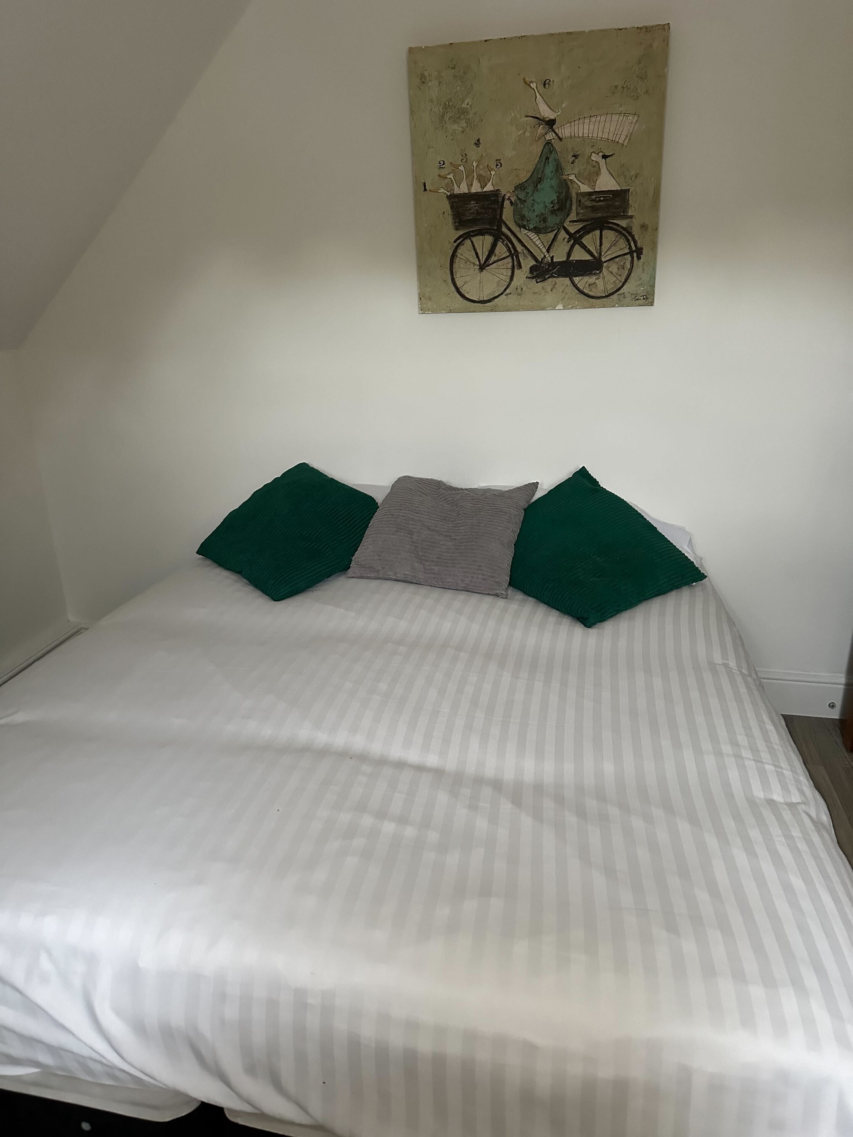 A bedroom with a bed, green and gray pillows, and a wall-mounted painting of a bicycle.