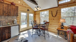 A cozy cabin interior with a stone fireplace, wooden walls, a dining area with chairs, and a sofa. - Cliffside Eureka Springs Cabin w/ Beaver Lake View (Eureka Springs)