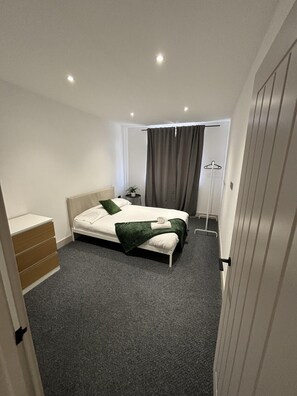 A modern hotel room with a single bed, a bedside table, a small plant, and a wardrobe. - 2bed Apt Benfleet - Familyfriendly - Freeparking (Benfleet)