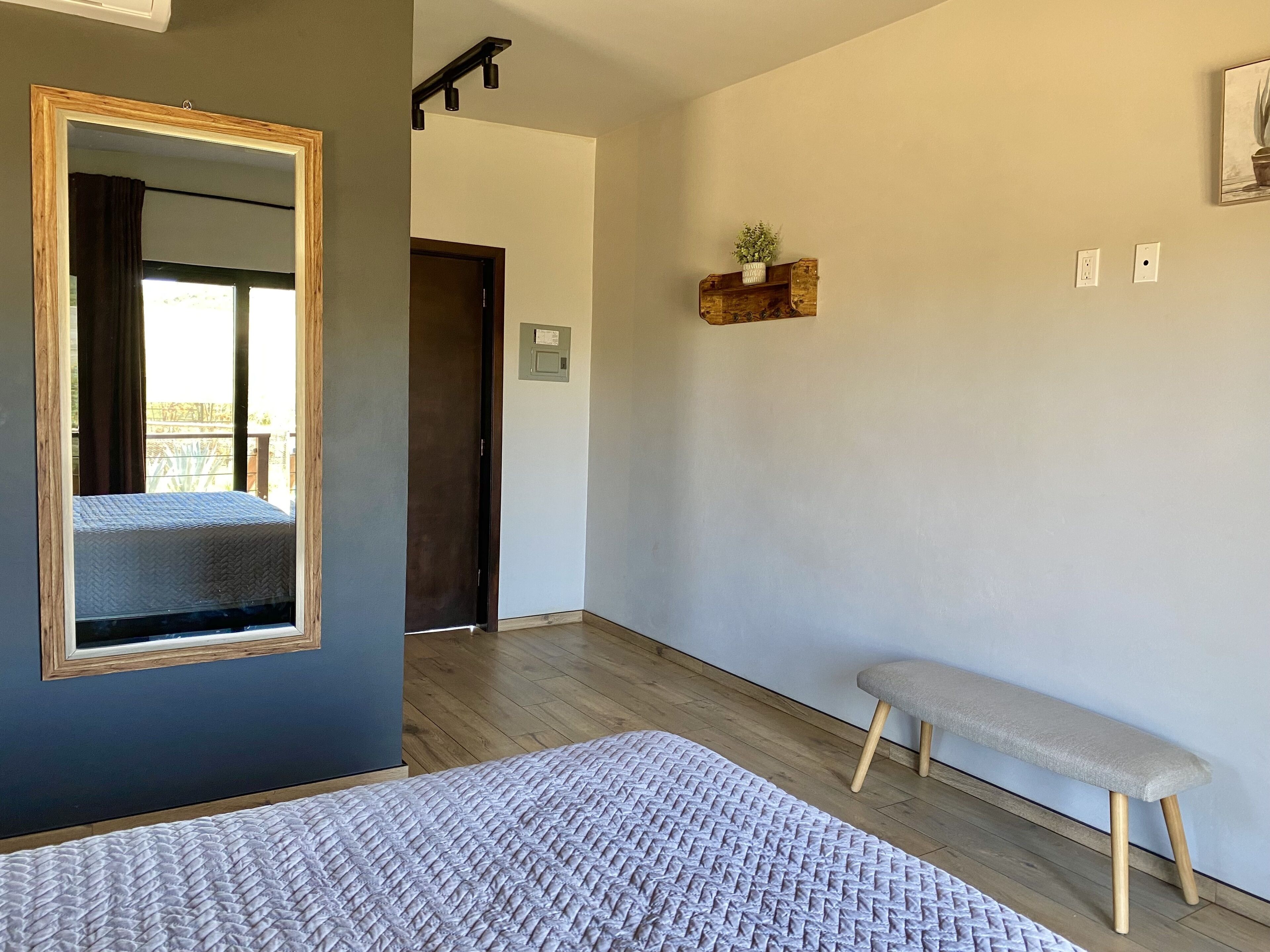Een slaapkamer met een grote spiegel, een bed, een bankje en een klein plankje met een plant.