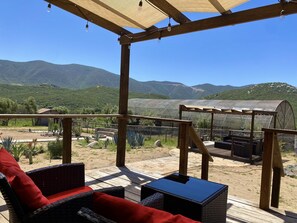 A covered outdoor seating area with a view of a greenhouse and mountains. - Coquenas del Valle (Valle de Guadalupe)