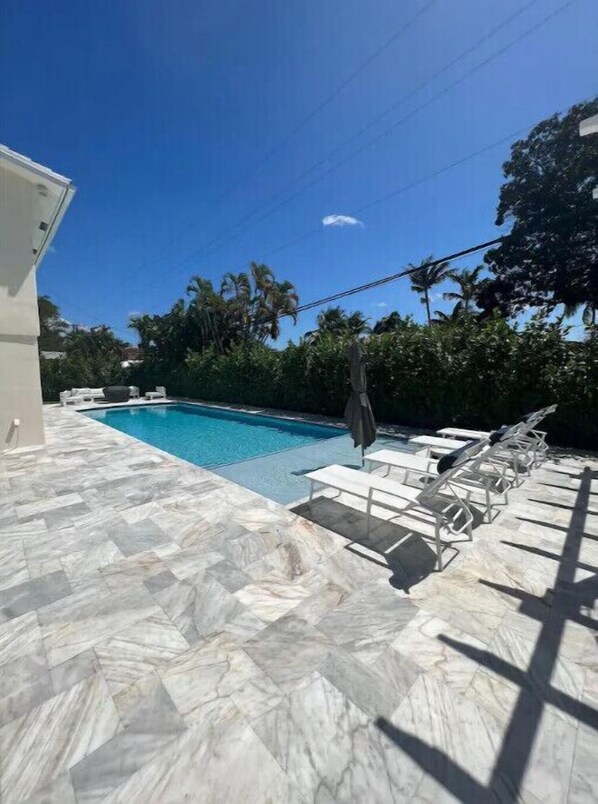 Relax by the clear blue pool surrounded by lush greenery and palm trees.