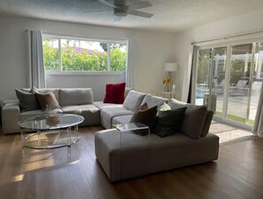 Relax in this spacious living room with a large sofa, flat-screen TV, and sliding glass door to an outdoor area with a pool.